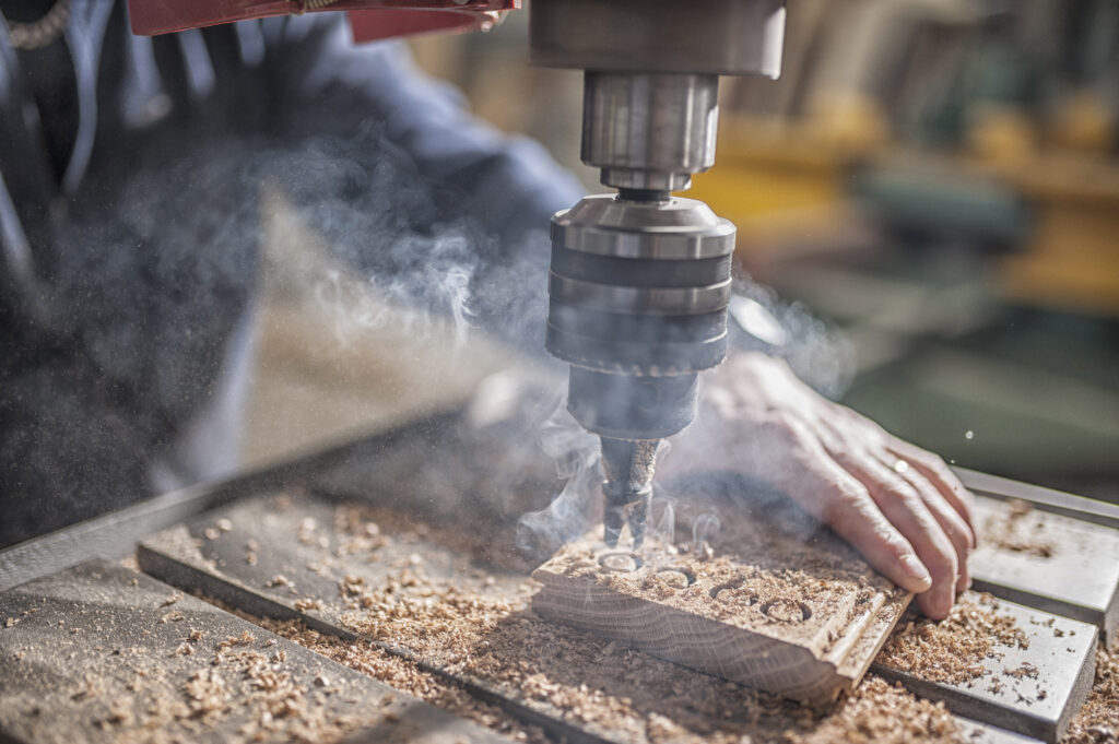 A carpenter drills holes into a floorboard plank.