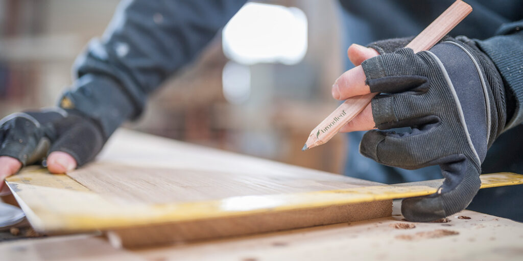 A carpenter using a pencil to mark wooden planks.
