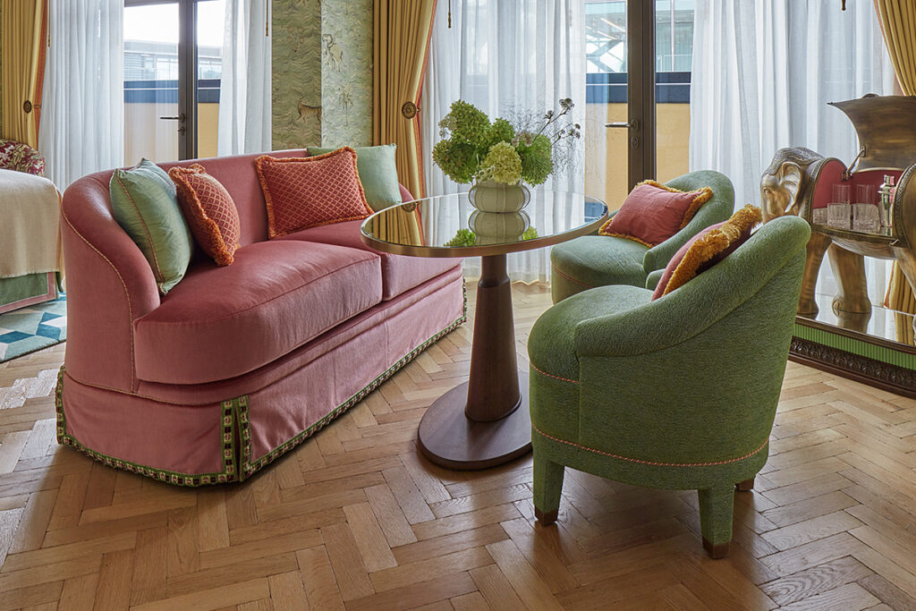 Herringbone pattern parquet flooring in a bedroom suite with pink sofa and green chair