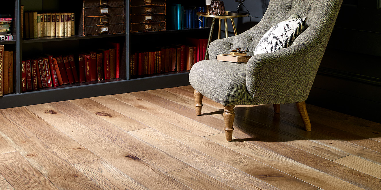 Rustic Broadleaf oak plank floor laid in a library room with grey armchair and black bookshelves.